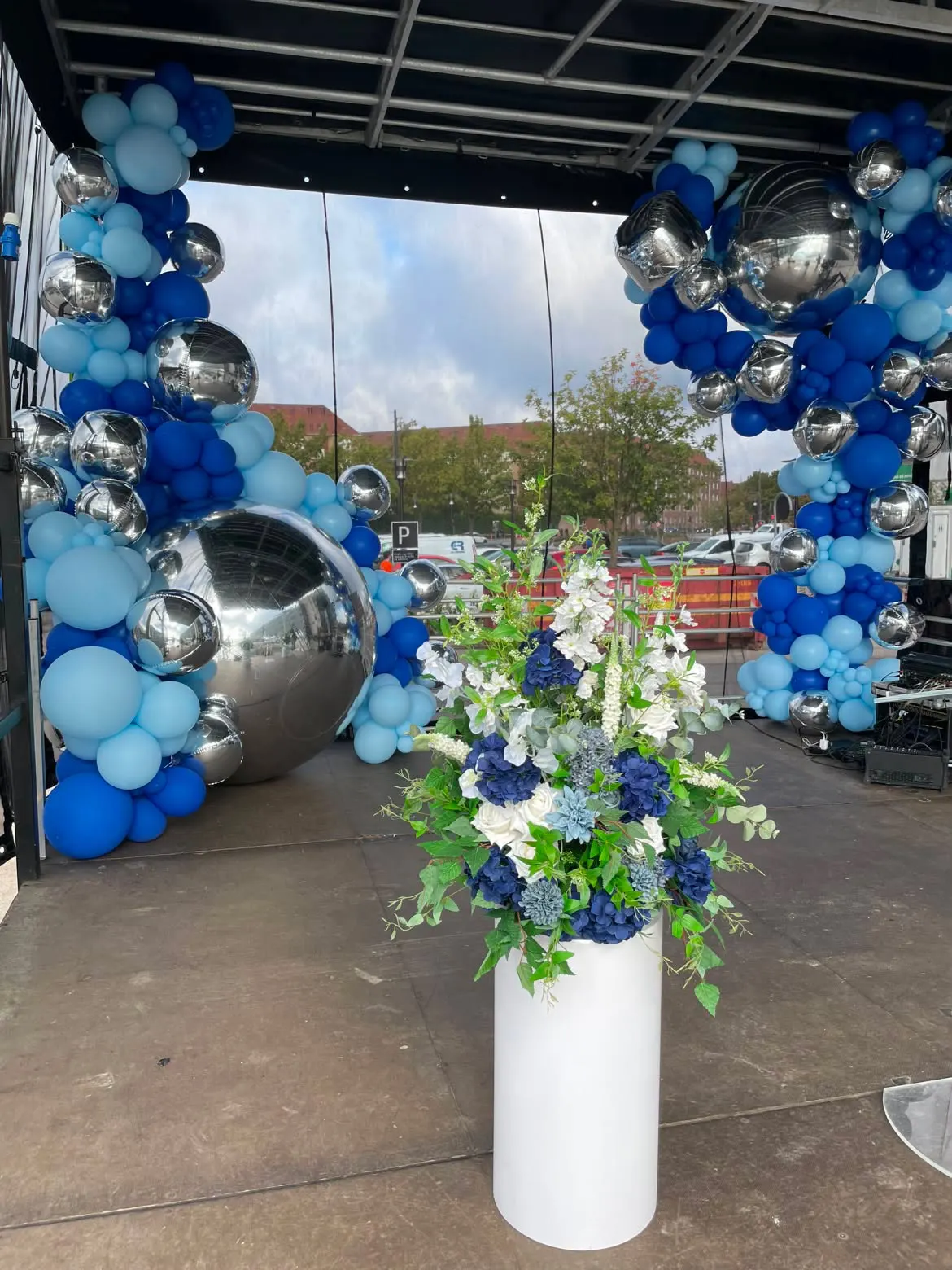 Blomsteropsætning med hvide roser og marineblå hortensia på hvid søjle foran ballondekoration