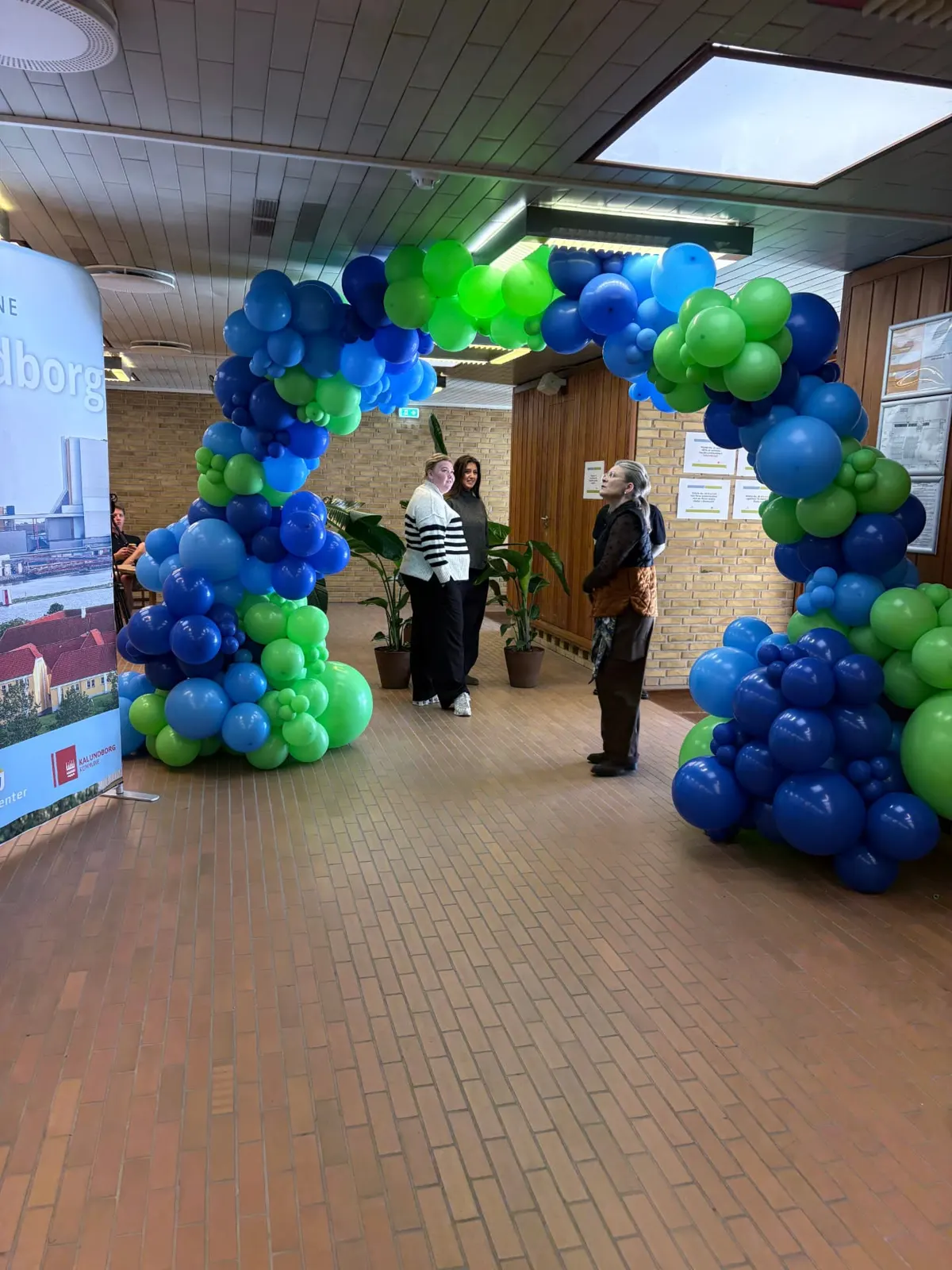 Gæster under ballonporten i grøn og blå ved indgangen til messen