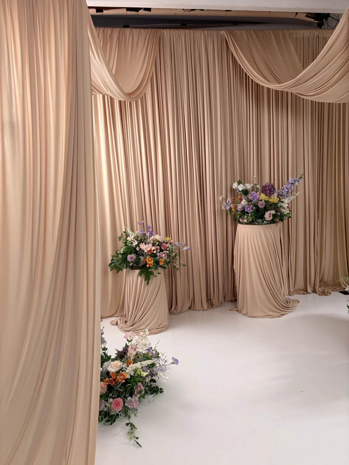 Gardinvæg i sand med draperinger, podier og blomsterarrangementer i fotostudiet