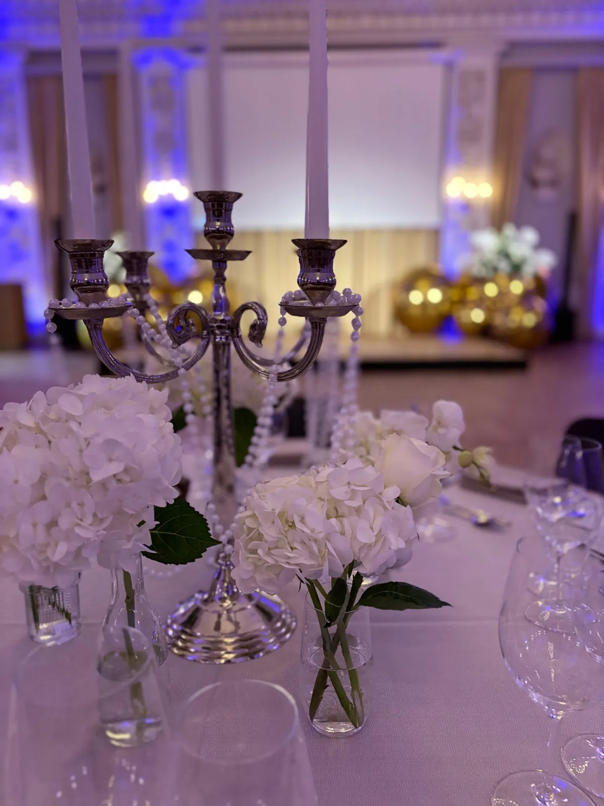 Sølvlysestage med perlekæder og hvide hortensia i små glasvaser som bordpynt