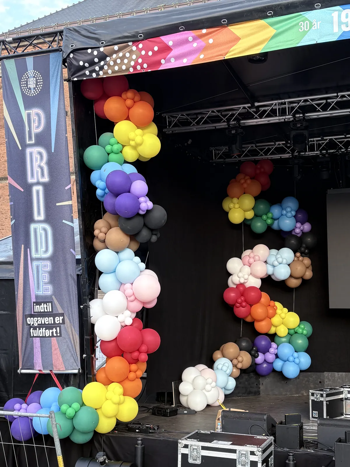 Organisk ballonguirlande i alle Pride-farverne op langs scenens truss ved Pride-banneret